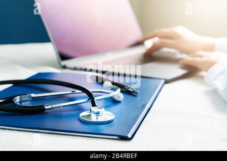 Stethoskop mit Akte und Laptop auf dem Schreibtisch, Arzt, der im Krankenhaus arbeitet und ein Rezept, Gesundheitswesen und medizinisches Konzept schreibt Stockfoto