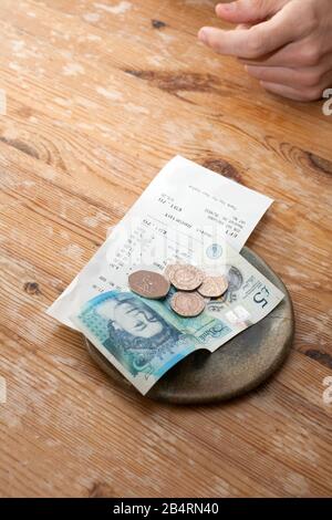 Eine Rechnung und ein Trinkgeld blieben in einem Restaurant mit englischem Geld auf dem Tisch Stockfoto