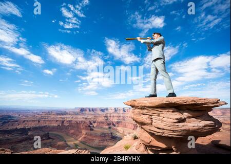 Ein langer Blick auf den im Freien stehenden Geschäftsmann, der durch das Teleskop über der dramatischen Wüstenlandschaft blickt Stockfoto