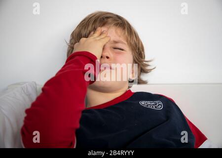 Kind mit Kopfschmerzen, Junge 9 Jahre alt, mit Schmerzen verzerrtes Gesicht, symbolisches Bild, Stockfoto