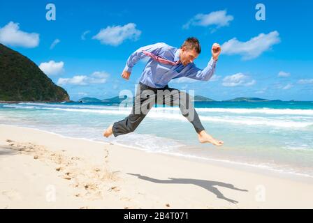 Barfuß-Geschäftsmann springt über einen leeren tropischen Strand Stockfoto
