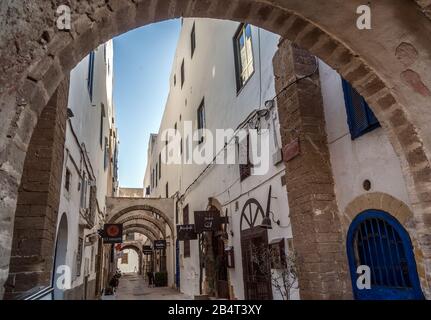 Bögen und Geschäfte an der Gasse von Medina entlang der Zinnen in Essaouira. Die Stadt ist als UNESCO-Weltkulturerbe registriert. Stockfoto