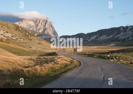 Kurvenreiche Straße auf dem Campo imperatore, die im Hintergrund am Herbstmorgen in den Abruzzen, Italien, zum Bergkorngrande führt Stockfoto