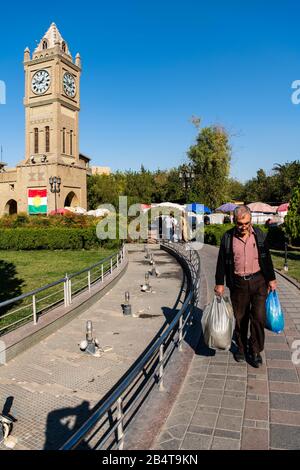 Irak, Iraq Kurdistan, Arbil, Erbil. Auf dem Park Shar läuft ein irakisch-kurdischer Mann eine Gasse. Im Hintergrund steht Erbil Uhr. Stockfoto