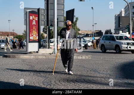 Irak, Iraq Kurdistan, Arbil, Erbil. Nerxt zum Park Shar ein irakisch-kurdischer Mann überquert die Straße, die in traditioneller kurdischer Kleidung gekleidet ist. Stockfoto