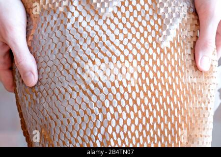 Hält ein Objekt in der Hand, verpackt in braunem Papier mit Löchern. Netzverpackung. Aus Sicherheitsgründen. Ansicht von oben. Stockfoto