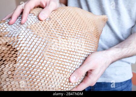 Hält ein Objekt in der Hand, verpackt in braunem Papier mit Löchern. Netzverpackung. Aus Sicherheitsgründen. Stockfoto