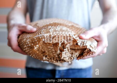 Hält ein Objekt in der Hand, verpackt in braunem Papier mit Löchern. Netzverpackung. Aus Sicherheitsgründen. Stockfoto