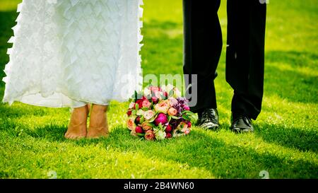 Füße und Schuhe frisch vermählt auf Gras im Garten und brautstrauß. Stockfoto