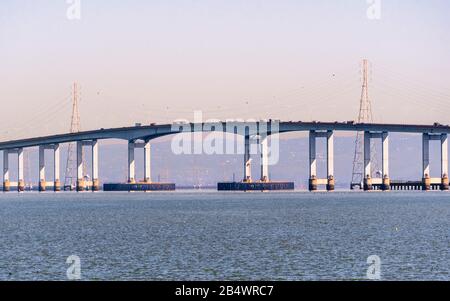 Nahaufnahme eines Teils der San Mateo Bridge, die die Halbinsel und die East Bay in der San Francisco Bay Area, Kalifornien, verbindet; Stromtürme und Stromleitungen V Stockfoto