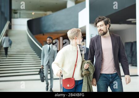 Fröhlicher junger Mann und Frau plaudern, während sie auf der Flughafenhalle spazieren, horizontaler mittlerer langer Schuss, Kopierraum Stockfoto