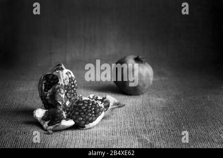 Schwarz-Weiß-Granatapfel und Rohgranaten auf Sacktuchhintergrund. Rustikaler Stil. TTasty Fruit Retro STILL LIFE dunkles Foto Stockfoto
