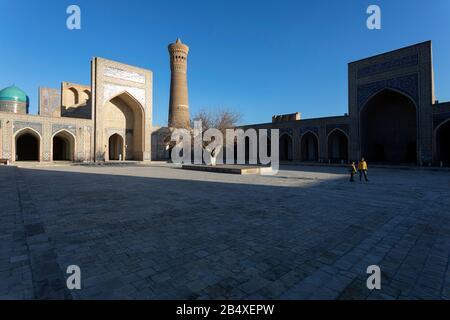 Mutter und Sohn im Innenhof mit Baum vor dem reich verzierten iwan und Kalon Minarett in der Kalon Moschee, Buchara Usbekistan Stockfoto