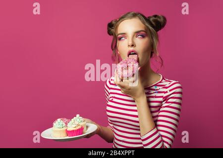 Hübsche Frau, die einen Donut leckt. Lustige Mädchen auf pinkfarbenem Hintergrund Stockfoto