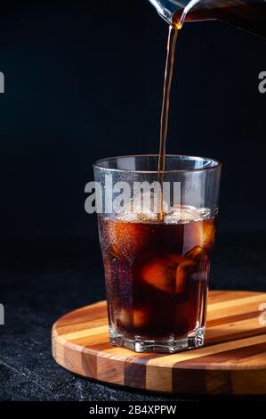 Iced Cola oder Cold Coffee Gießen in Großes Glas auf dunklem Hintergrund. Konzept Erfrischendes Sommergetränk. Stockfoto