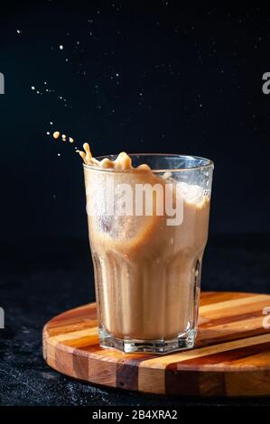 Iced Coffee with Splash in Tall Glass on Dark Background. Konzept Erfrischendes Sommergetränk. Stockfoto