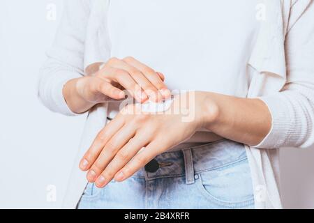 Weibliche Hände reiben kosmetische Creme in die Haut, Nahaufnahme. Junge Frau tragen Feuchtigkeitscreme auf weißem Studiohintergrund auf. Stockfoto