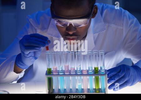 Horizontales Nahaufnahme Porträt junger männlicher Wissenschaftler am Schreibtisch im modernen Labor, das mit Flüssigkeiten in Reagenzgläsern arbeitet Stockfoto