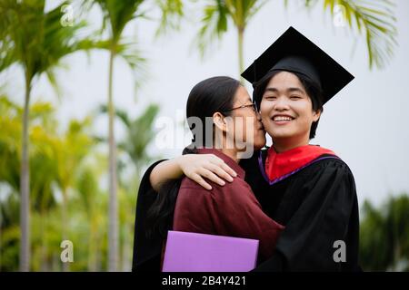 Abschlussfeier. Junge Hochschulabsolventin, die sich mit ihrer Mutter umarmt, gratuliert der Studentin an der Universität. Stockfoto