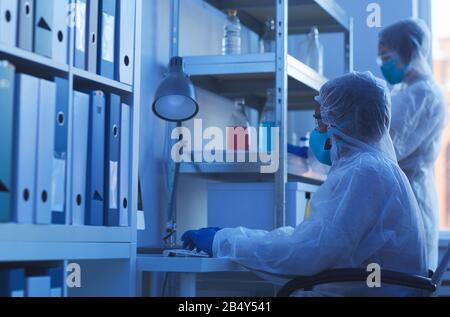 Horizontale Seitenansicht von zwei nicht erkennbaren medizinischen Wissenschaftlern in Schutzanzügen, die in modernen Labors arbeiten Stockfoto
