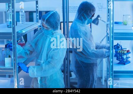 Horizontaler, mittlerer, hoher Winkelschuss von zwei nicht erkennbaren Wissenschaftlern in Schutzanzügen, die einen neuen Impfstoff entwickeln Stockfoto