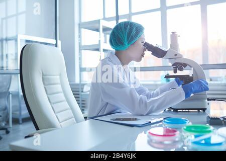 Horizontales Mittelseitenporträt junger asiatischer Wissenschaftlerinnen, das den Flüssigkeitsinhalt mit Mikroskop analysiert, Kopieraum Stockfoto
