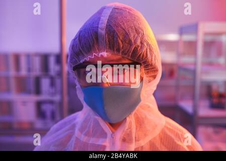 Horizontales Kopf- und Schulterporträt unkenntlich junger Frau mit Laboranzug, Brille und Maske mit Blick auf die Kamera, Kopie Spac Stockfoto