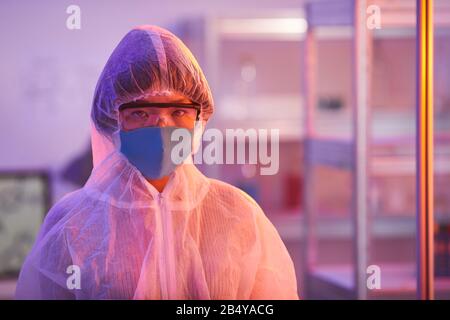 Horizontales Mittel-Nahaufnahme-Porträt von jungen Menschen, die eine schützende Laboruniform tragen, mit Blick auf Kamera, Rosa und gelbes Licht Stockfoto