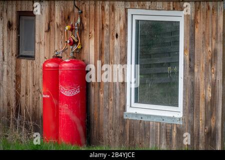 An der Außenwand eines kleinen Holzhauses befinden sich zwei große rote Gasflaschen zum Erhitzen Stockfoto