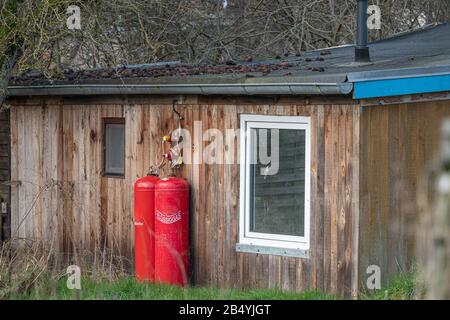 An der Außenwand eines kleinen Holzhauses befinden sich zwei große rote Gasflaschen zum Erhitzen Stockfoto