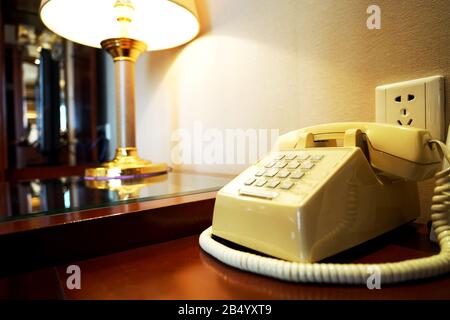 Altes Telefon auf Holztisch in der Nähe von Wand und Rampe im Hotelzimmer Stockfoto