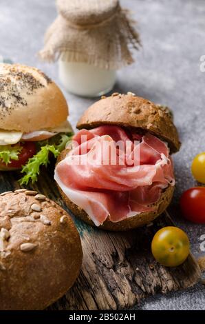 Knuspriger Burger mit Schinken in Scheiben auf einem Vintage-Holzschneidebrett. Dunkles, stimmungsvolles Speisefoto, gut für Bar-Menüs und Poster. Stockfoto