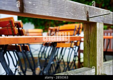 Blick durch ein Holzterrassengeländer zu Tischen und gefalteten Stühlen eines Restaurants bei schlechtem Wetter. Stockfoto