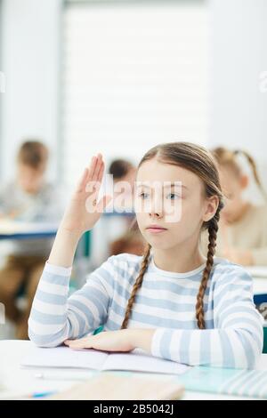 Das vertikale Porträt der intelligenten Grundschule ehrt Schüler, die am Schulschalter sitzen und die Hand in den Unterricht heben, den Kopierraum Stockfoto