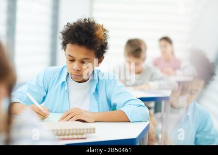 Horizontales mittleres Porträt des nachdenklichen afroamerikanischen Sitzens im Klassenzimmer Arbeit an Unterrichtsaufgabe, Kopierraum Stockfoto