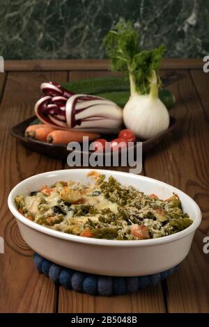 Glutenfreie Kasserolle (Pasta al Forno) mit Gemüse und Käse auf einem Holztisch. Stockfoto