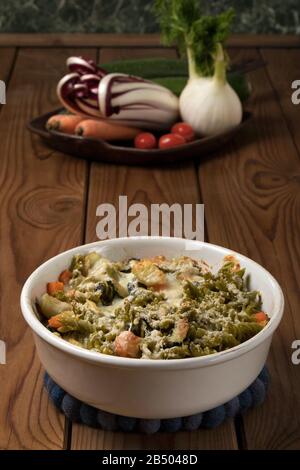 Glutenfreie Kasserolle (Pasta al Forno) mit Gemüse und Käse auf einem Holztisch. Stockfoto