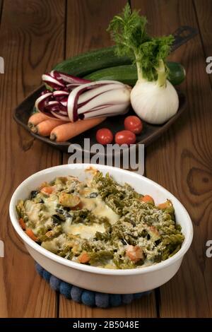Glutenfreie Kasserolle (Pasta al Forno) mit Gemüse und Käse auf einem Holztisch. Stockfoto