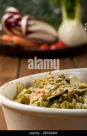 Glutenfreie Kasserolle (Pasta al Forno) mit Gemüse und Käse auf einem Holztisch. Stockfoto