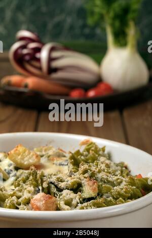 Glutenfreie Kasserolle (Pasta al Forno) mit Gemüse und Käse auf einem Holztisch. Stockfoto