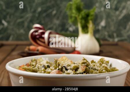 Glutenfreie Kasserolle (Pasta al Forno) mit Gemüse und Käse auf einem Holztisch. Stockfoto