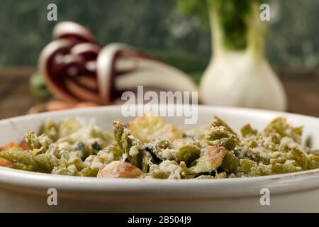 Glutenfreie Kasserolle (Pasta al Forno) mit Gemüse und Käse auf einem Holztisch. Stockfoto