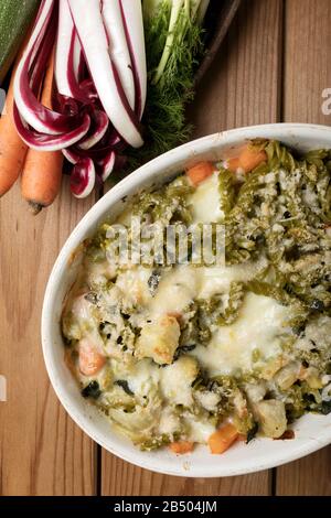 Glutenfreie Kasserolle (Pasta al Forno) mit Gemüse und Käse auf einem Holztisch. Stockfoto