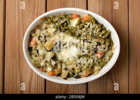 Glutenfreie Kasserolle (Pasta al Forno) mit Gemüse und Käse auf einem Holztisch. Stockfoto