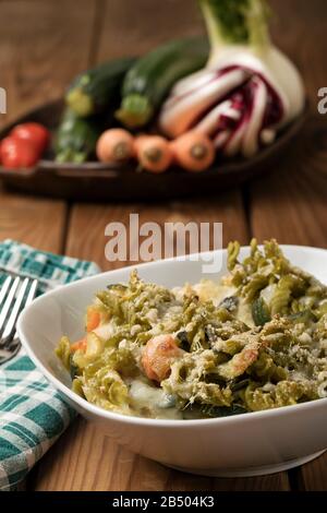 Glutenfreie Kasserolle (Pasta al Forno) mit Gemüse und Käse auf einem Holztisch. Stockfoto