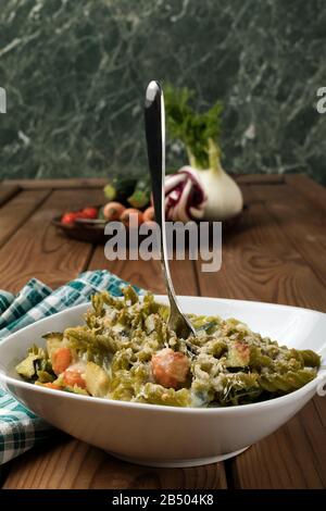 Glutenfreie Kasserolle (Pasta al Forno) mit Gemüse und Käse auf einem Holztisch. Stockfoto