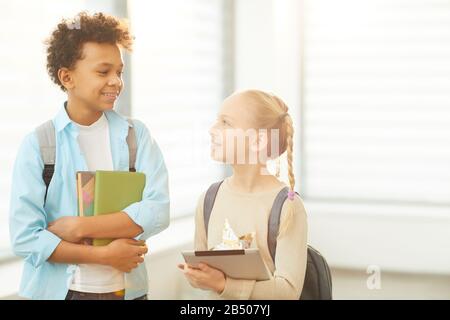 Horizontales Mittelporträt zwei Klassenkameraden, die im Schulflur stehen und sich während der Pause über etwas unterhalten, Kopieraum Stockfoto