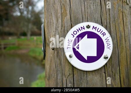 Schild für den John Muir Way, einen Fernwanderweg in Schottland. Auf Holzpfosten mit verschwommenem Hintergrund Stockfoto