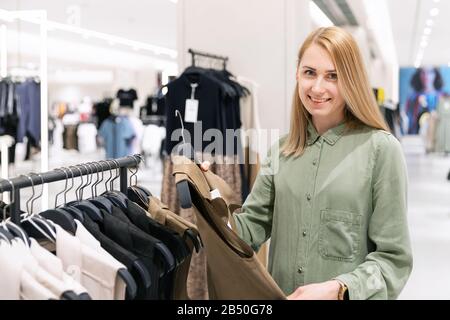 Fröhliche junge Frau wählt Kleidung in einem Einkaufszentrum Stockfoto
