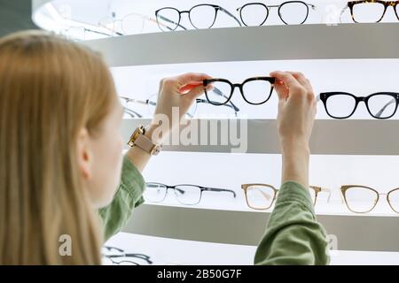 Frau wählt eine Brille aus dem Regal im Optikladen Stockfoto